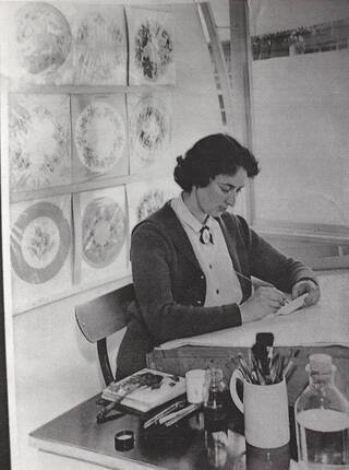 Black and white photograph of woman sat at desk writing something on paper